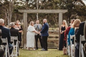 A bride and groom stand under a timber arbor at their Ottimo House wedding ceremony