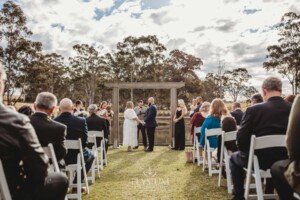 A bride and groom stand under a timber arbor at their Ottimo House wedding ceremony