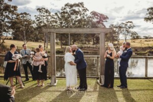 A bride and groom kiss under a timber arbor at their Ottimo House wedding ceremony