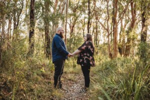 An engaged couple hold hands while standing on a dirt track in bushland