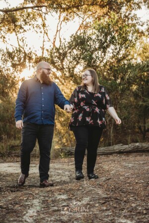An engaged couple hold hands while walking along a dirt track in bushland