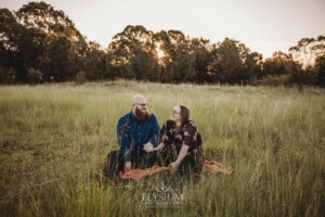 A couple sit on a picnic rug in a long grassy field at sunset
