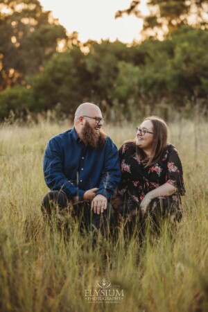 A couple sit on a wooden log in a long grassy field at sunset