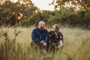 A couple sit on a wooden log in a long grassy field at sunset