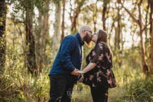 An engaged couple hold hands while standing on a dirt track in bushland