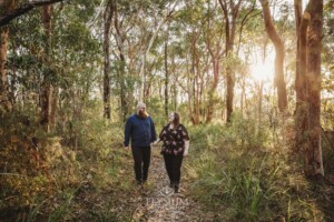 An engaged couple hold hands while walking along a dirt track in bushland
