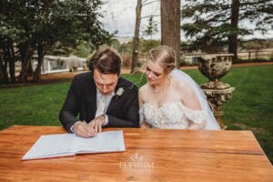 A bride and groom sign their marriage certificate during their outdoor wedding ceremony
