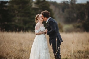 A bride and groom share a kiss as they stand in a field at Bendooley Estate