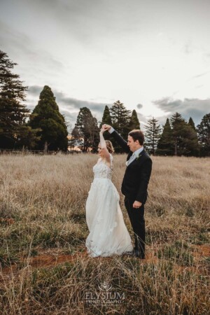 A groom twirls his bride as they dance in a grassy field at Bendooley Estate