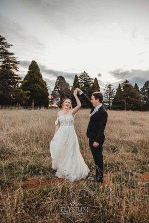 A groom twirls his bride as they dance in a grassy field at Bendooley Estate