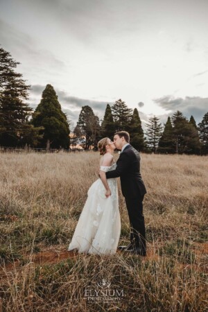 A bride and groom share a kiss as they stand in a field at Bendooley Estate