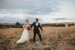 A bride and groom walk holding hands through the grass at Bendooley Estate