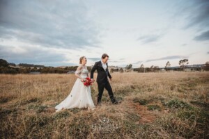 A bride and groom walk holding hands through the grass at Bendooley Estate
