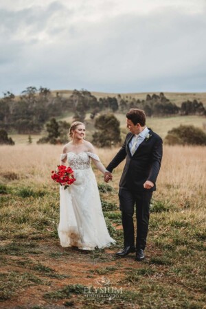 A bride and groom walk holding hands through the grass at Bendooley Estate