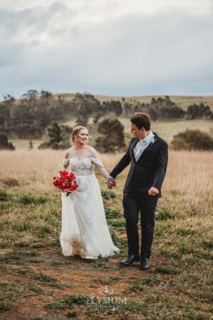 A bride and groom walk holding hands through the grass at Bendooley Estate