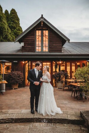 A bride and groom stand in front of the Bendooley book barn linking arms