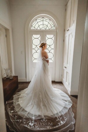 A bride stands in front of a large white door with a large bridal gown flowing across the floor