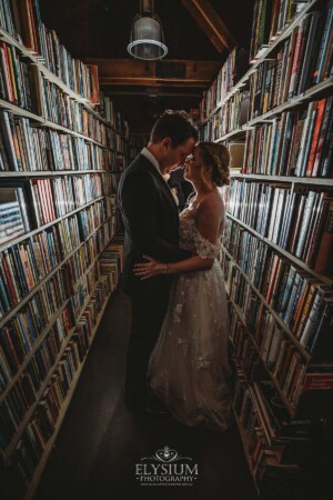 A bride and groom standing amongst the bookshelves at Bendooley Estate with a flash lighting them from behind