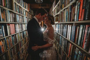 A bride and groom standing amongst the bookshelves at Bendooley Estate with a flash lighting them from behind