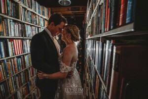 A bride and groom standing amongst the bookshelves at Bendooley Estate with a flash lighting them from behind