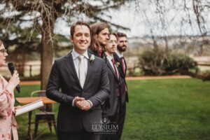 A groom awaits his bride standing at the front of the wedding ceremony