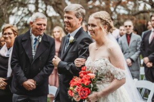 A bride walks down the aisle to greet her groom during their outdoor wedding ceremony