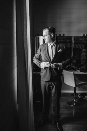 A black and white image of a groom buttoning up his suit as he prepares for the wedding at Burnham Grove