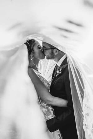 A couple share a kiss as they stand under the bridal veil at sunset