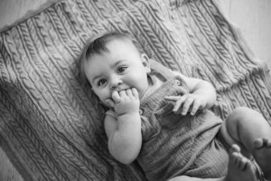 A baby bot lays on a knitted blanket and sucks his fingers