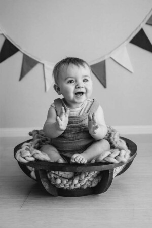 A baby boy sits in a round bowl clapping his hands and smiling for a milestone session