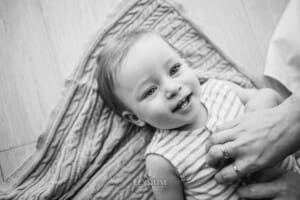 A baby boy laying on a blanket smiles as his mother tickles him