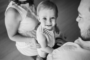 A baby boy sits between his parents in a bright studio for his first birthday session