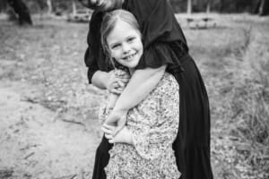 A little girl smiles as her mothers arms wrap around her