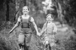 Two girls hold hands as they run together along a bushy track