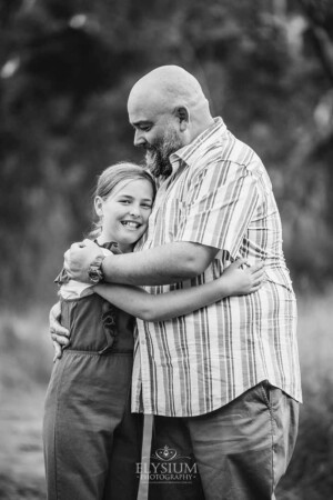 A girl hugs her father asn they stand in a grassy field at sunset