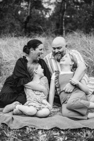 A family sit on a blanket and cuddle in a grassy field