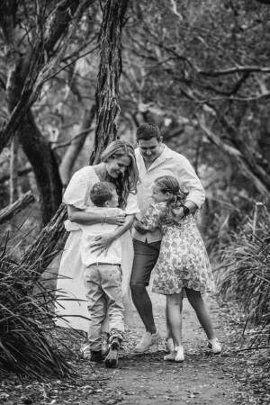A family photo in black and white of parents cuddling their children on a bush track