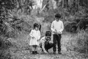 Three children draw in the dirt with sticks on a bush track