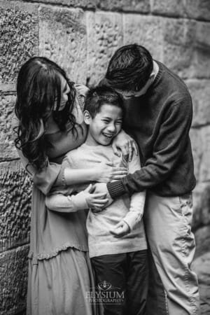 Parents cuddle their son between them as they tickle him and laugh