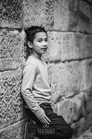 A boy stands against a sandstone wall with his hands in his pockets