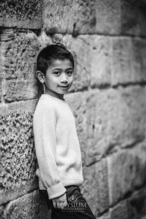 A little boy stands against a stone wall and smiles for a portrait