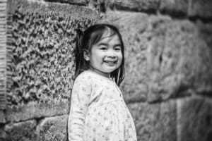 Black and white photo of a little girl standing against a sandstone wall