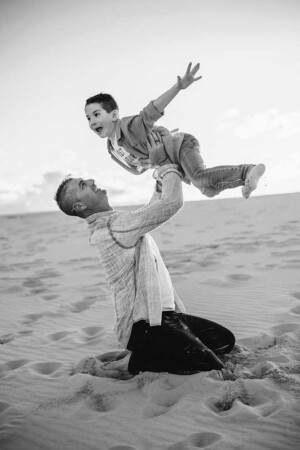 A father hoists his son above him as they play and laugh during a beach family photo session