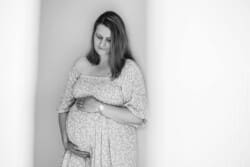 A pregnant woman stands in a bright room holding her round belly looking down at her tummy