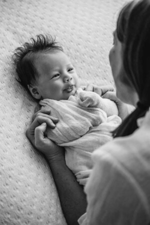 A newborn baby pokes his tongue out as he smiles up at his mother