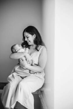 A mother cradles her newborn baby in her arms and smiles down at him