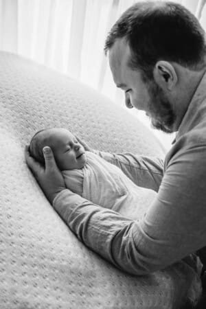 A newborn baby smiles as he is held by his father's hands on a white blanket