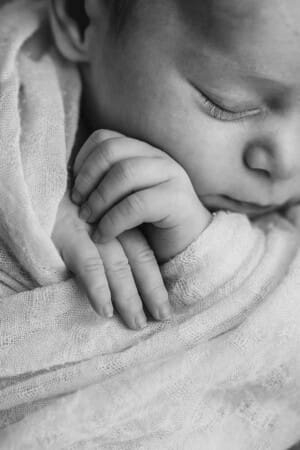 Black and white detail photo of a newborn baby's hands folded over the white wrap