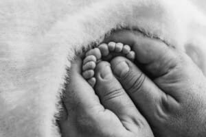 A fathers big hands hold the tiny toes of his newborn baby