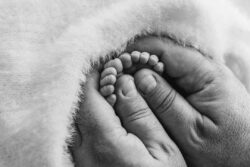 A fathers big hands hold the tiny toes of his newborn baby